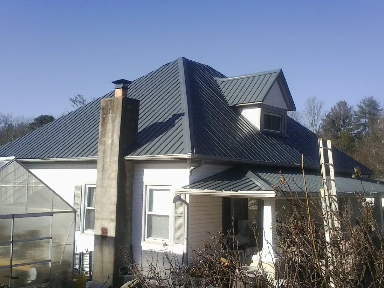 Dark blue standing seam metal roof on a white farmhouse with dormer — Slate & Tile Roof Repair by Roofing Brothers in Calhoun Falls