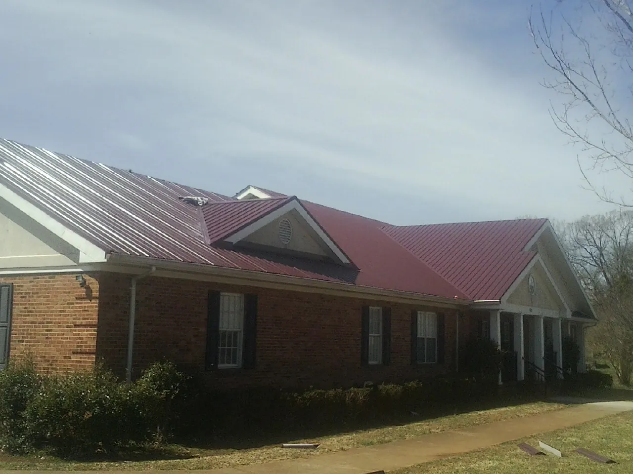 Red metal roof with gabled entries on a long brick building, from a Hail Damage Roof Repair job in Calhoun Falls