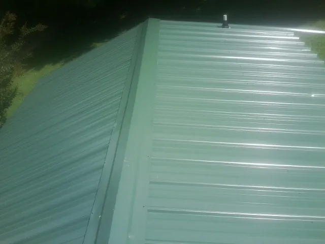 New green metal panels meeting at the ridge of a roof — Flat Roof Repair work by our crew in Calhoun Falls