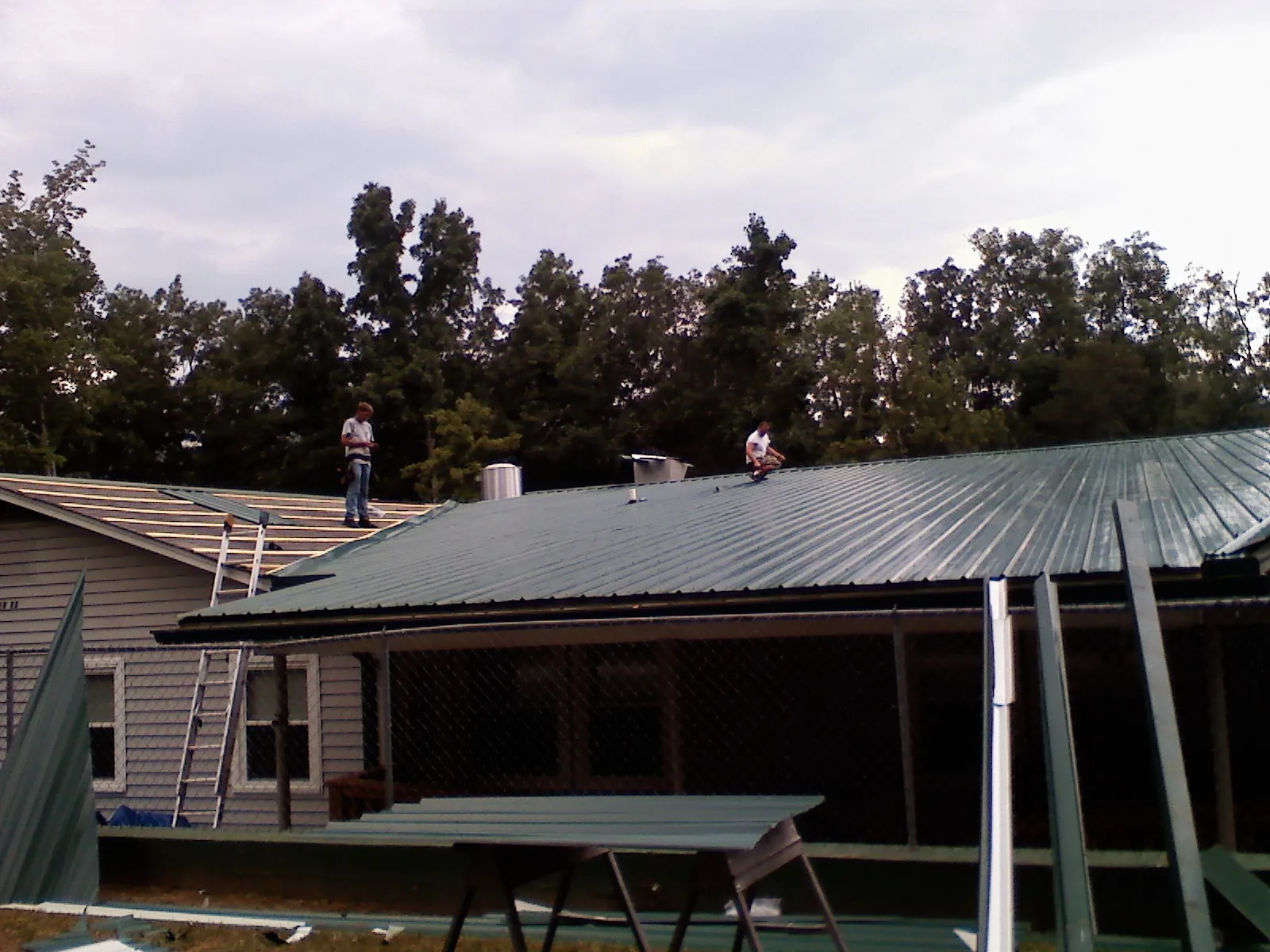 Two roofers installing green metal panels above a covered porch in Calhoun Falls