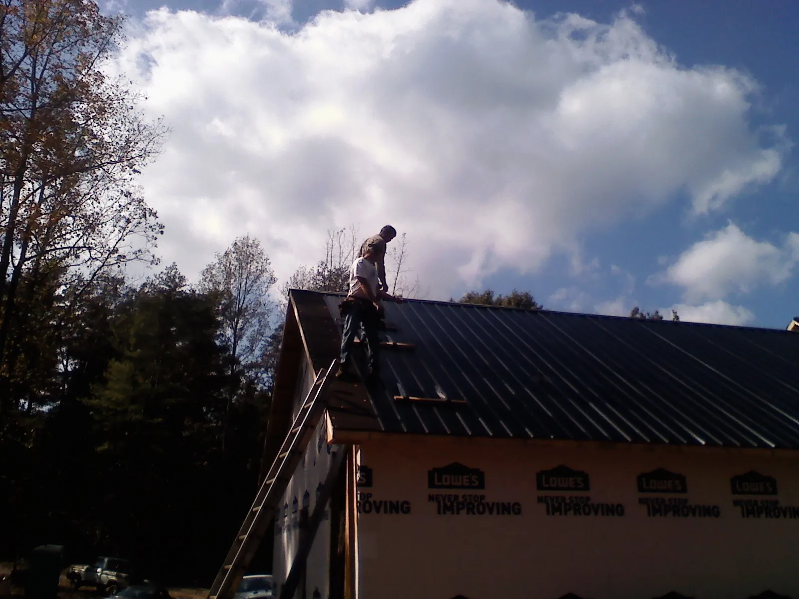 Roofer fastening dark metal panels high against a cloudy sky, from a Roof Inspection job in Calhoun Falls