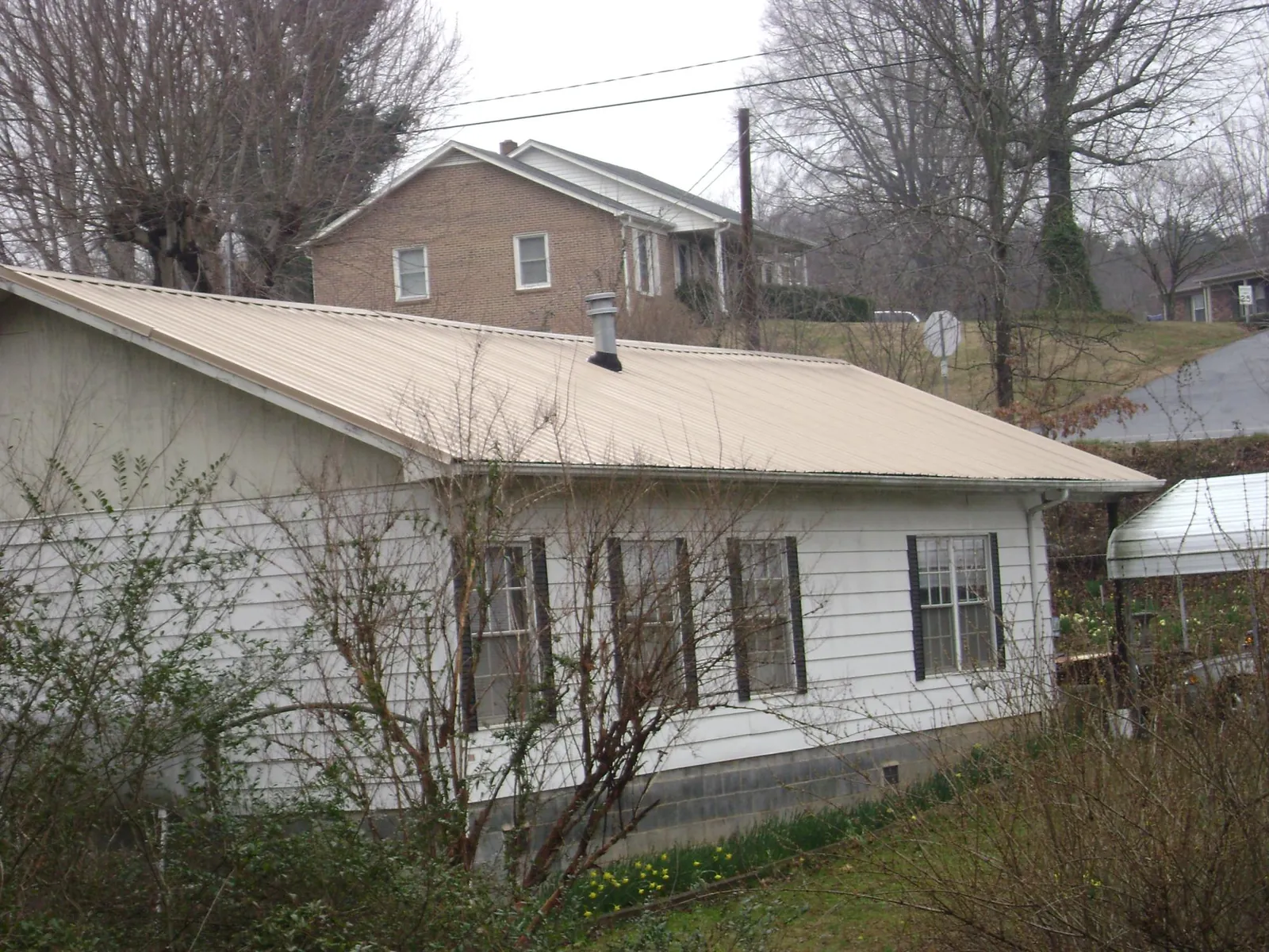 Tan metal roof on a white sided house set into a hillside — Commercial Roofing by Roofing Brothers in Calhoun Falls